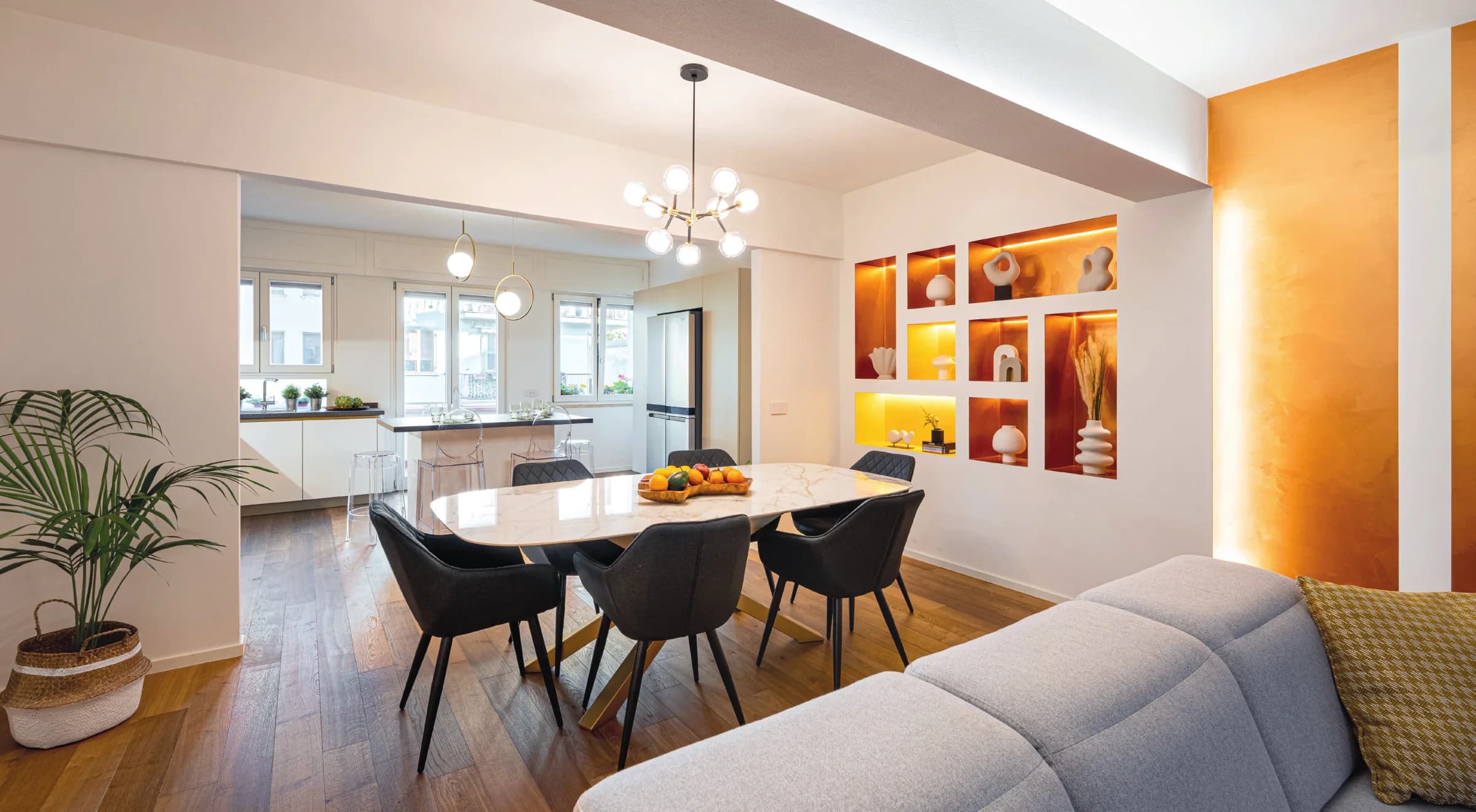 Geometria cromatica: la sala da pranzo open space si distingue per l'armonia tra il marmo del tavolo, il calore delle nicchie bronzate e il contrasto deciso delle sedie nere.